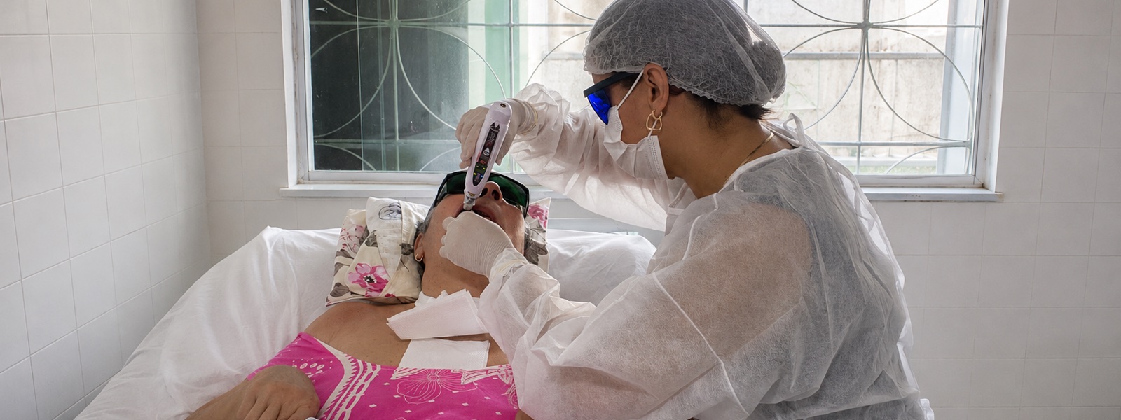 Aplicação de laserterapia em paciente deitada, durante atendimento fora do consultório